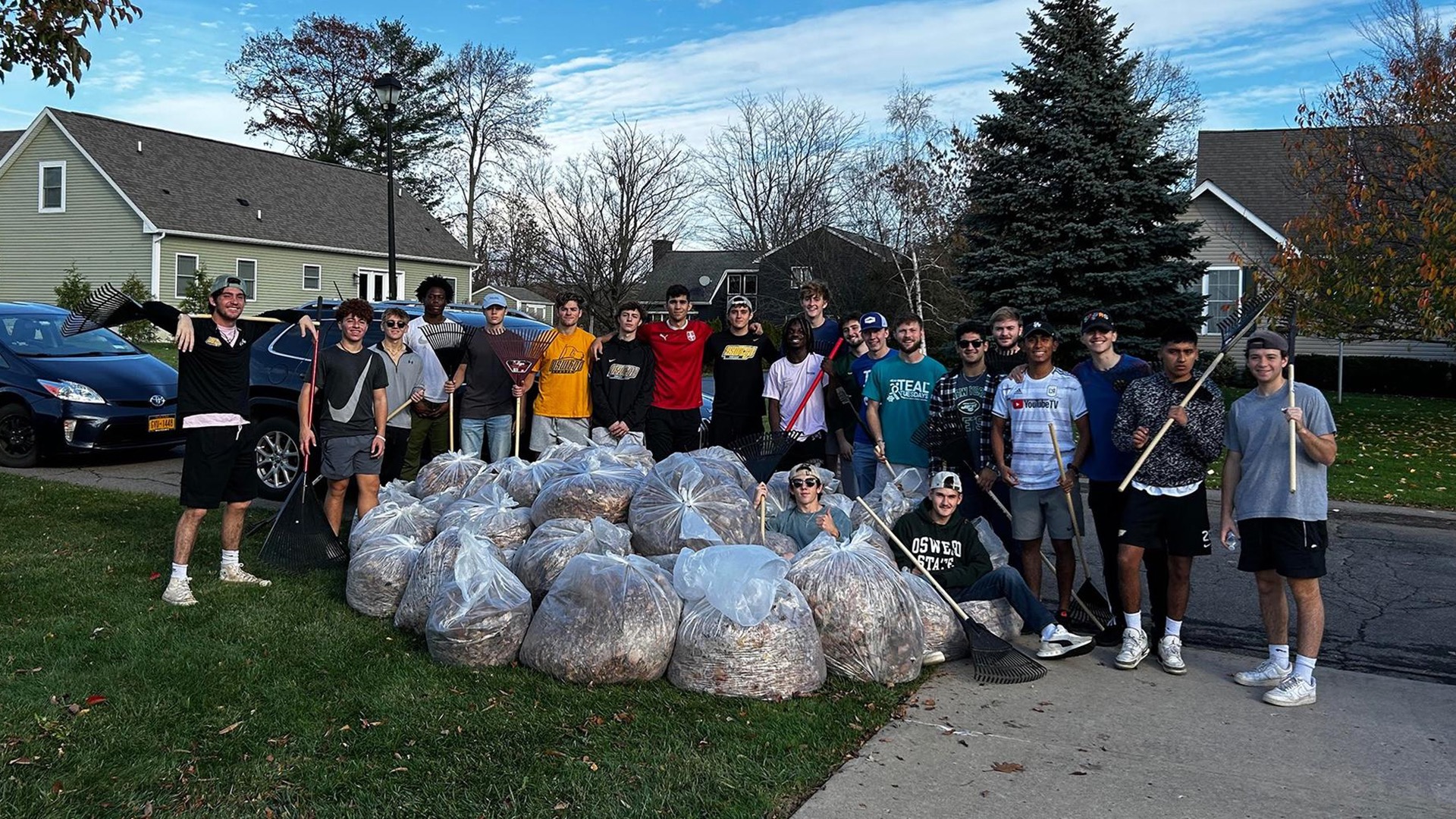 The Oswego State men's soccer team stands next to a pile of leaves 