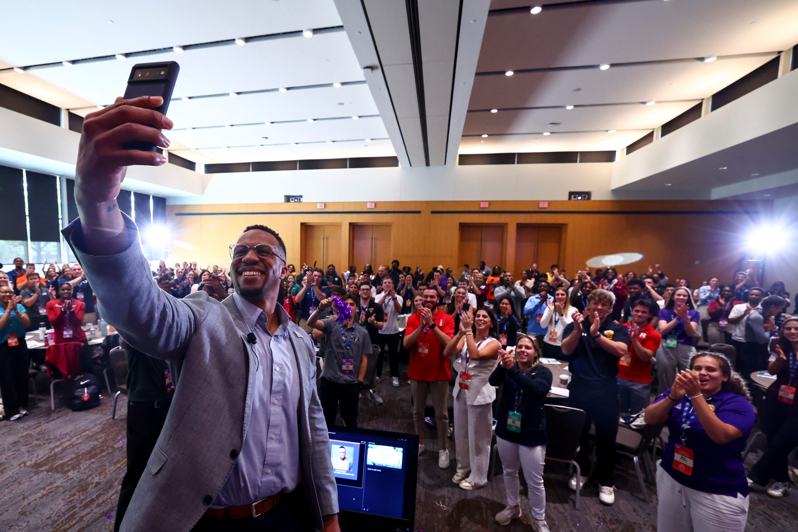 A man takes a selfie with a large crowd of student-aged people.