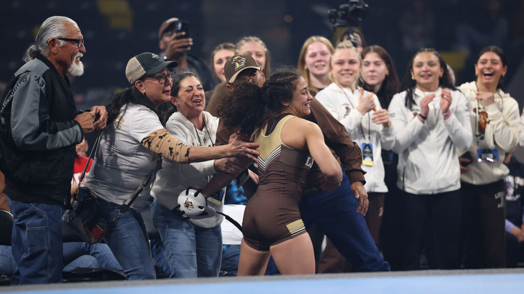 Jimenez celebrates her 110-pound title at the National Collegiate Women’s Wrestling Championships with her family as her teammates cheer. (Photo by Justin Tafoya / NCAA Photos)