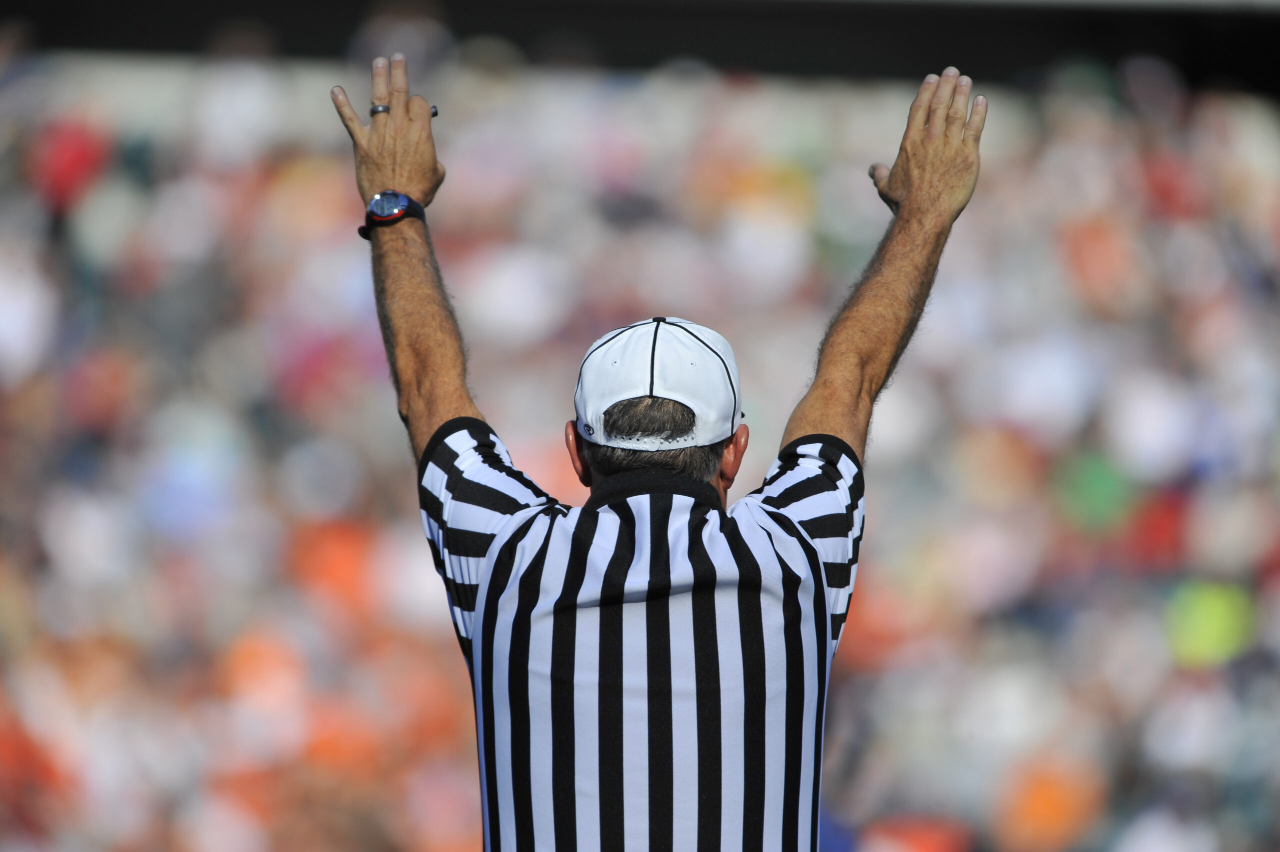 Referee holding his arms straight up indicating a call has been made in front of a blurred out background of a crowded stadium